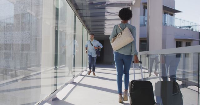 Man and woman walking through an airport terminal carrying luggage. Perfect for portraying business travel, holiday trips, or transportation services in a modern setting.