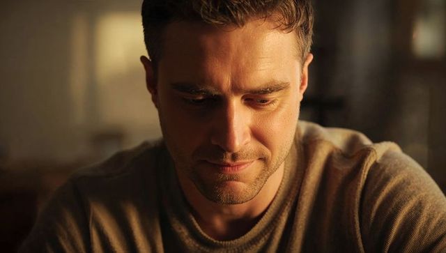 Man gazing downward in warm light, contemplative portrait capturing quiet reflective mood