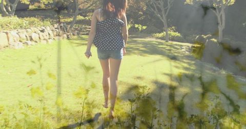 Walking barefoot across sunlit backyard lawn in polka-dot top and denim shorts