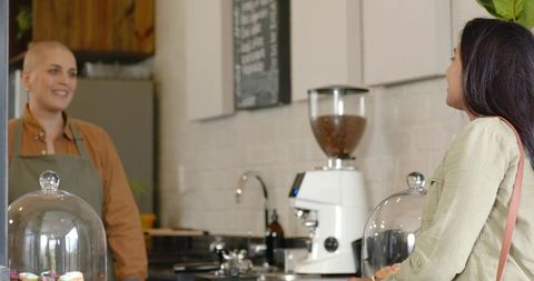 Barista smiling while serving indian customer at cozy cafe counter with pastries