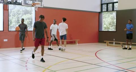 Multiethnic men playing pickup basketball in indoor gym practicing teamwork and fitness