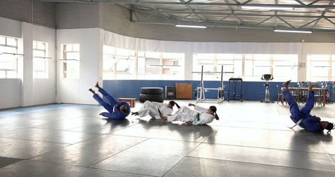 Teenagers perfecting backward judo rolls in professional martial arts class