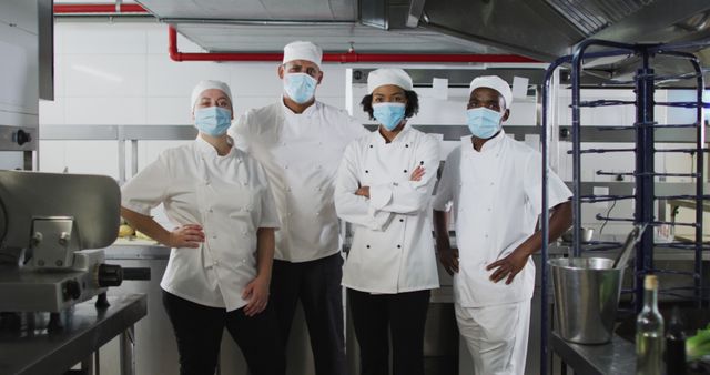 Portrait of diverse group of chefs wearing face masks standing in restaurant kitchen. Health and hygiene in restaurant kitchen during coronavirus covid 19 pandemic.