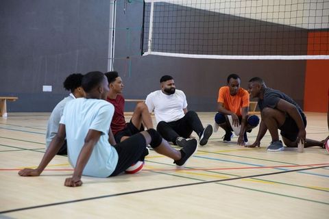 African american men resting and talking on indoor gym court, teamwork and camaraderie