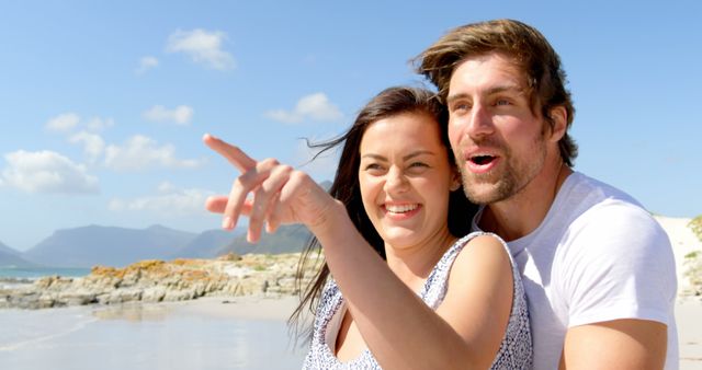 Captures happy couple at beach on sunny day, woman pointing excitedly while man smiles. Excellent for travel promotions, vacation packages, romantic getaways, lifestyle blogs, or adverts highlighting joyful moments and relationships in nature-filled settings.