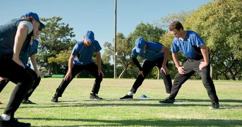 Men's baseball team warming up with coach leading agility drills on sunny training field