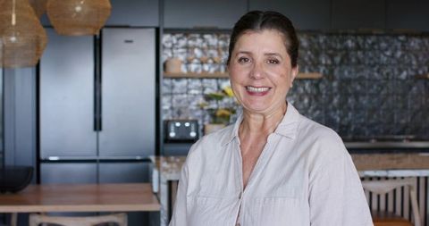 Smiling mature woman standing in modern minimalist kitchen near island counter home portrait