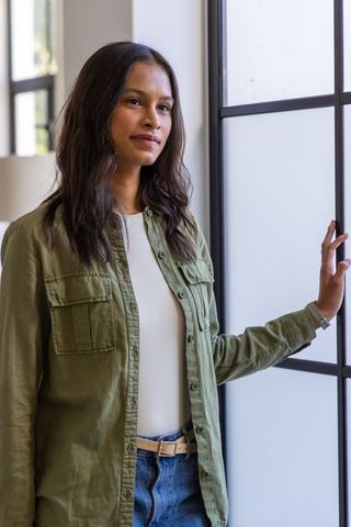 African woman standing beside frosted grid window in minimalist home wearing wristwatch