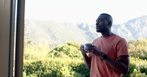 African American man breathing morning air on balcony holding mug enjoying mountain view