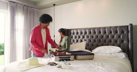 Joyful Couple Packing Suitcase for Vacation in Bedroom