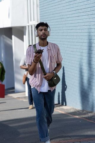 Asian man walking and listening to music on headphones carrying green crossbody bag