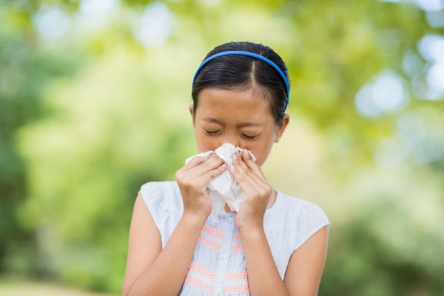Girl blowing her nose with handkerchief while sneezing in the park