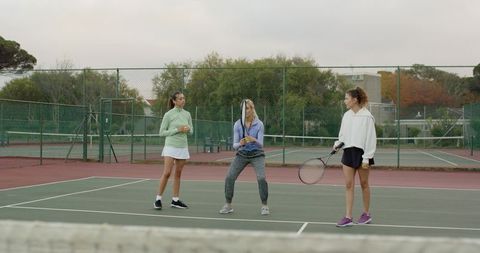 Three women practicing tennis on outdoor court during coaching session and drills