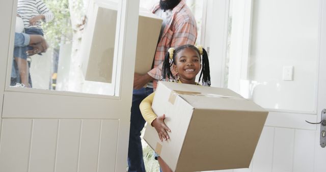 This stock photo showcases an African American family moving into their new home. A young girl carries a cardboard box enthusiastically while her father follows with another box. The scene embodies a fresh start, happiness, and the excitement of relocation. Ideal for use in advertisements, blog posts, or articles about real estate, moving services, family life, and starting anew.