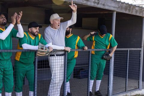 Veteran baseball coach raising finger calling play from dugout while players reacting