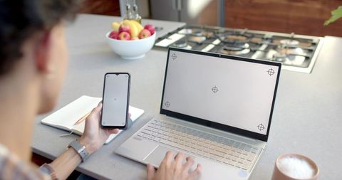 Man working from home using laptop and smartphone at modern kitchen island with notebook