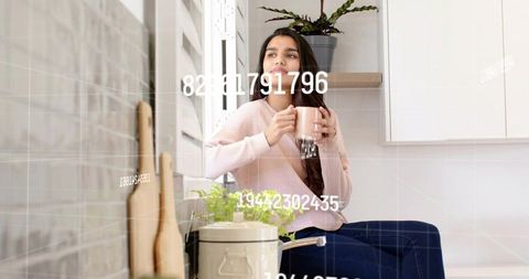 Relaxing indian woman sipping coffee by window in sunlit cozy kitchen showing data overlay