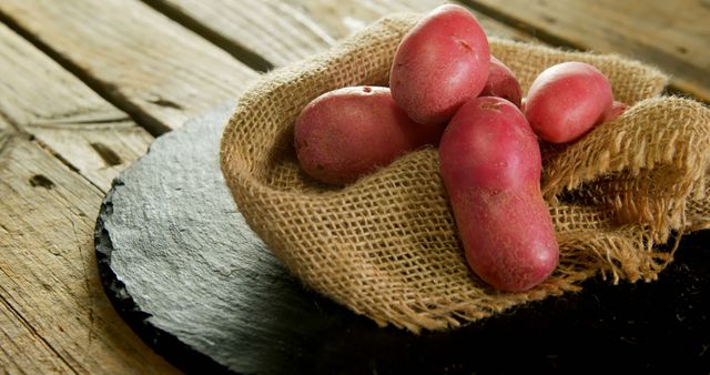 Red potatoes rest on a rustic burlap cloth atop a wooden surface, with copy space. Their smooth, unblemished skin suggests fresh produce perfect for culinary use.