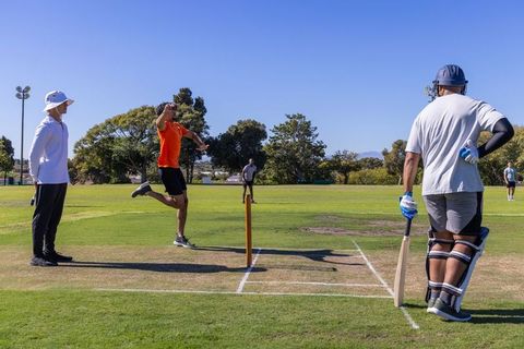 Fast bowler delivering ball to batsman on sunny grass cricket pitch