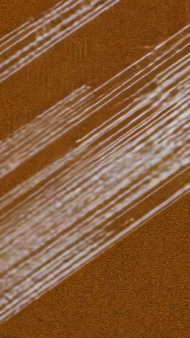 Vertical abstract texture video animating diagonal white streaks across brown grain