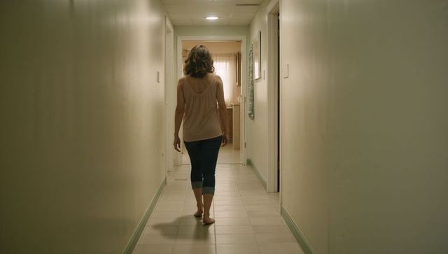 Woman walking barefoot down narrow hallway toward open doorway in warm minimalist interior