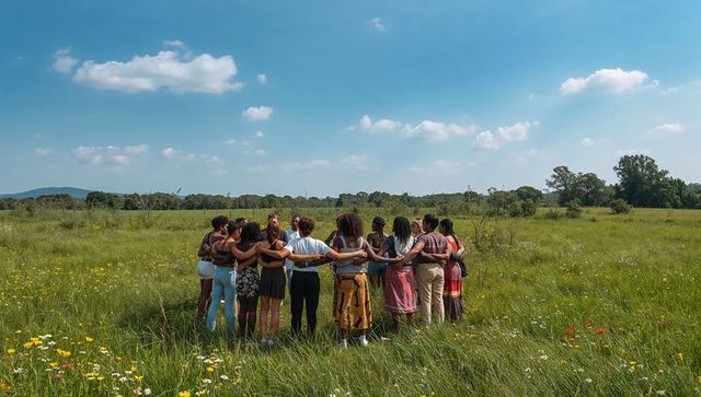 Women linking arms in wildflower meadow standing in circle embracing community