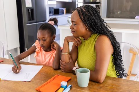 African mother guiding daughter with homework at kitchen table, family learning moment