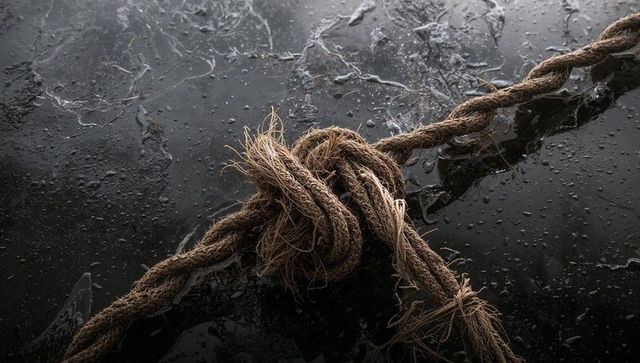 Weathered hemp rope knot on wet deck, frayed fibers and water droplets macro texture