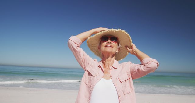 Happy senior caucasian woman wearing hat and sunglasses, smiling on beach. Senior lifestyle, realxation, nature, free time and vacation.