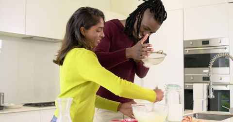 Diverse couple baking together in bright modern kitchen mixing batter and sifting flour