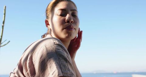 Turning woman closing eyes touching jaw by sunlit seaside horizon serene coastal portrait