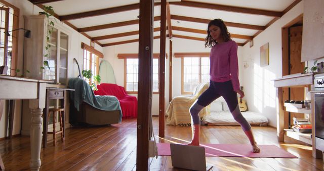 Relaxed biracial woman practicing yoga, standing and stretching in sunny cottage bedroom. simple healthy living in off the grid rural home.
