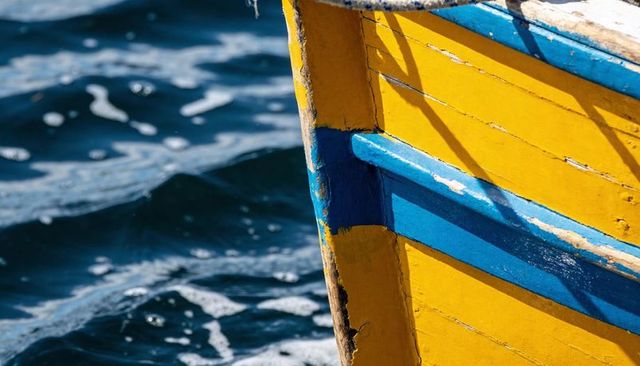 Sunlit yellow wooden boat bow with blue trim and peeling paint over deep sea waves