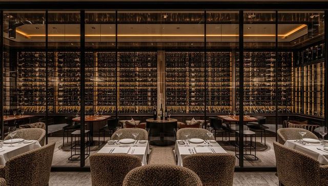 Luxury wine wall featuring backlit racks and intimate linen dining with woven armchairs