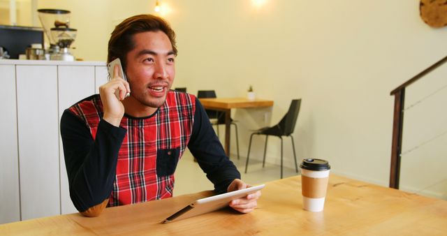 Casual Asian Man Talking on Smartphone in Café, Holding Tablet - Download Free Stock Images Pikwizard.com