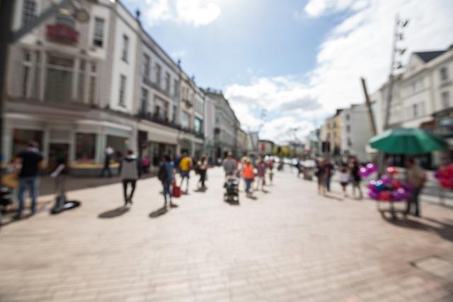 Blurred view of a busy street with pedestrians walking on a sunny day. Ideal for use in themes related to urban life, travel destinations, or graphic backgrounds.