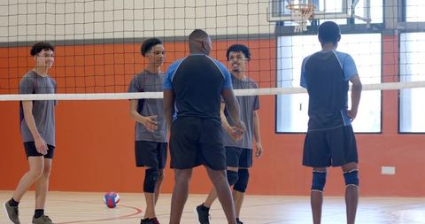 High school male volleyball team huddling at net with coach leading indoor gym practice