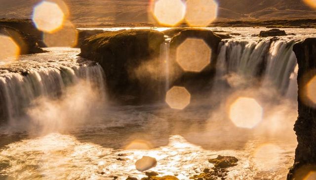 Golden sunlit waterfalls cascading over rocky gorge with mist and hexagonal lens flares
