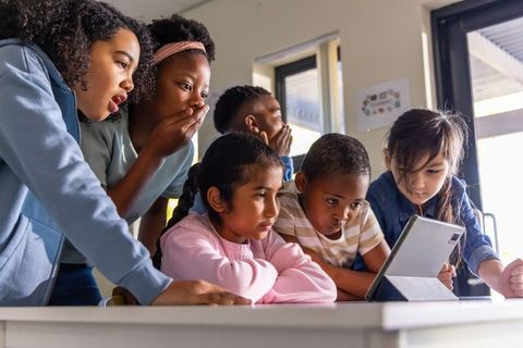 Elementary students leaning around tablet sharing curiosity and collaborative learning