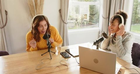 Two hosts recording cozy home podcast with headphones, microphones and laptop