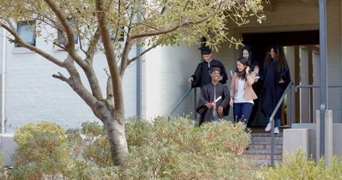 Diverse high school graduates walking down steps, holding diplomas