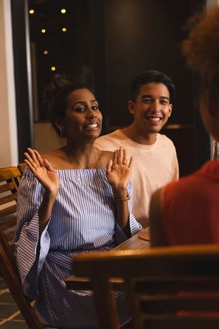 Couple enjoying cozy evening dining while friend gesturing menu choice