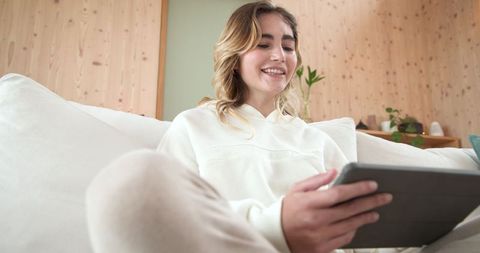 Smiling Woman Enjoys Relaxing with Tablet in Cozy Living Room
