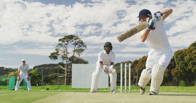 Cricket players in action on a sunny day with lush green field and blue sky in the background. Ideal for sports enthusiasts, advertisements, and articles related to cricket or team sports. This captures the intensity and focus of outdoor sports.