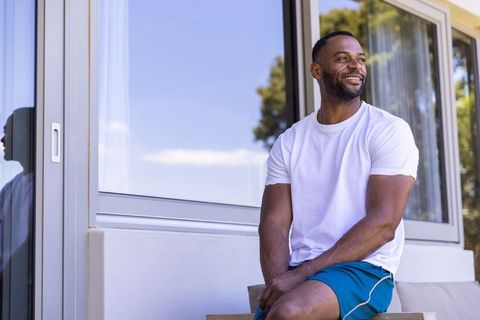 African man smiling and relaxing on modern patio bench in casual summer clothes at home