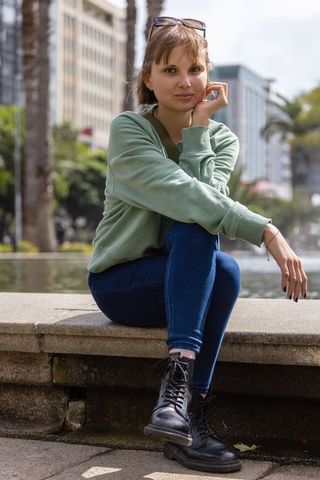 Young woman sitting by fountain in urban plaza wearing green hoodie and black boots