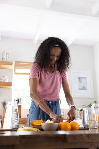 African american woman slicing oranges on kitchen island for fresh juice and wellness