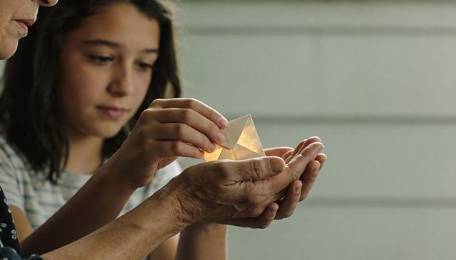 Teen placing glowing origami prism into elder cupped hands on porch, family moment