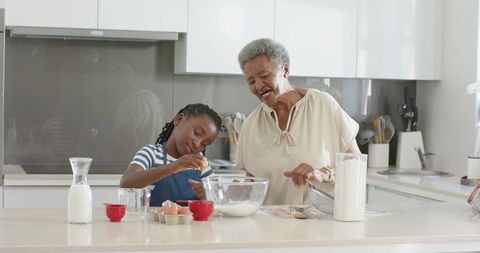African grandmother teaching granddaughter baking together in bright modern kitchen joyful