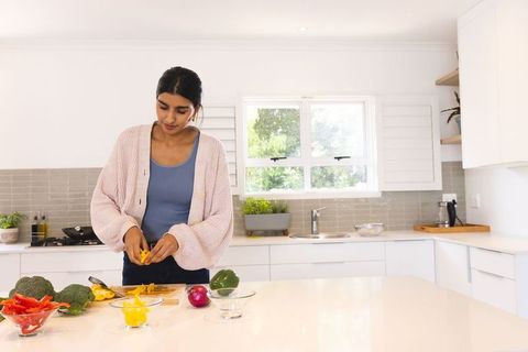 Woman preparing fresh yellow bell pepper in modern kitchen